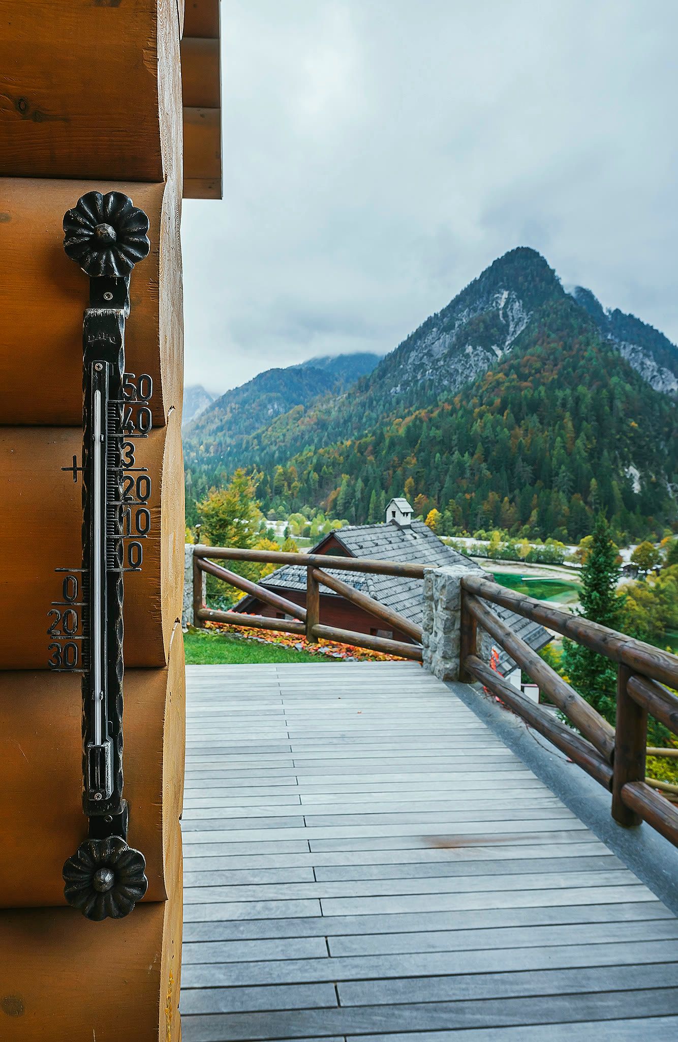 A balcony rail with an old thermometer, with a mountain peak visible beyond.