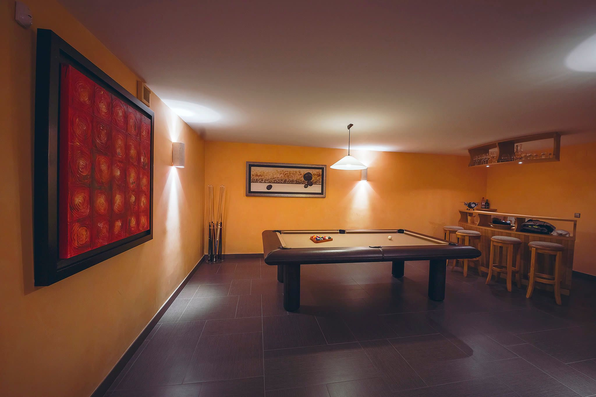 A wide view of the billiards room with a large red artwork, a bar, and stools.