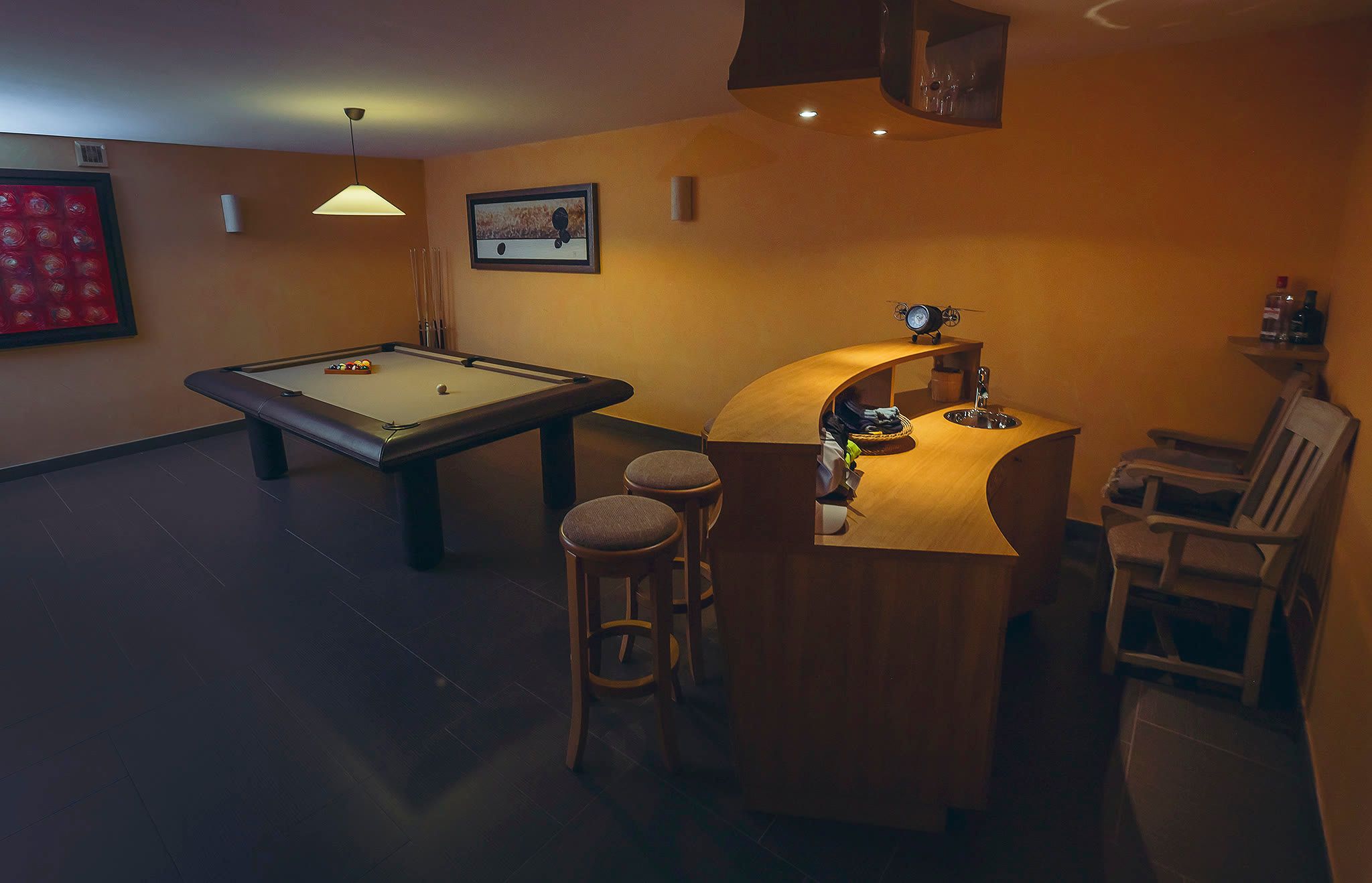 The billiards table with cues, bar stools beyond, and dark orange walls.