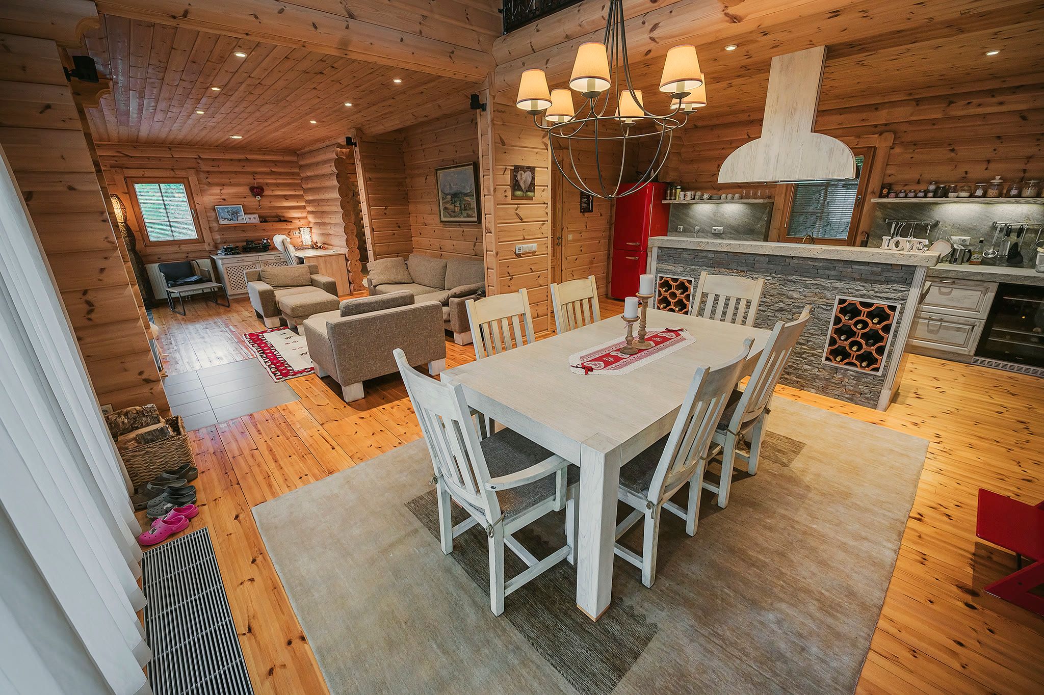 The open-plan living area with the dining table in the foreground and the kitchen and living room beyond, lit by a chandelier.