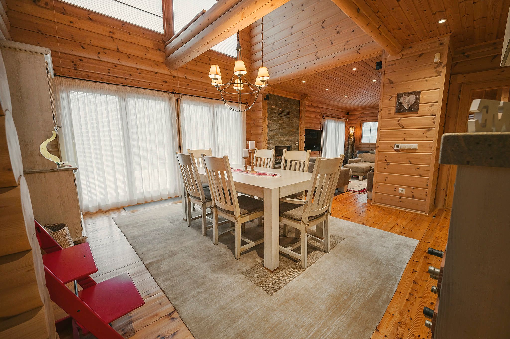 The dining table set beneath the vaulted log ceiling, with the gallery above and tall curtained windows.