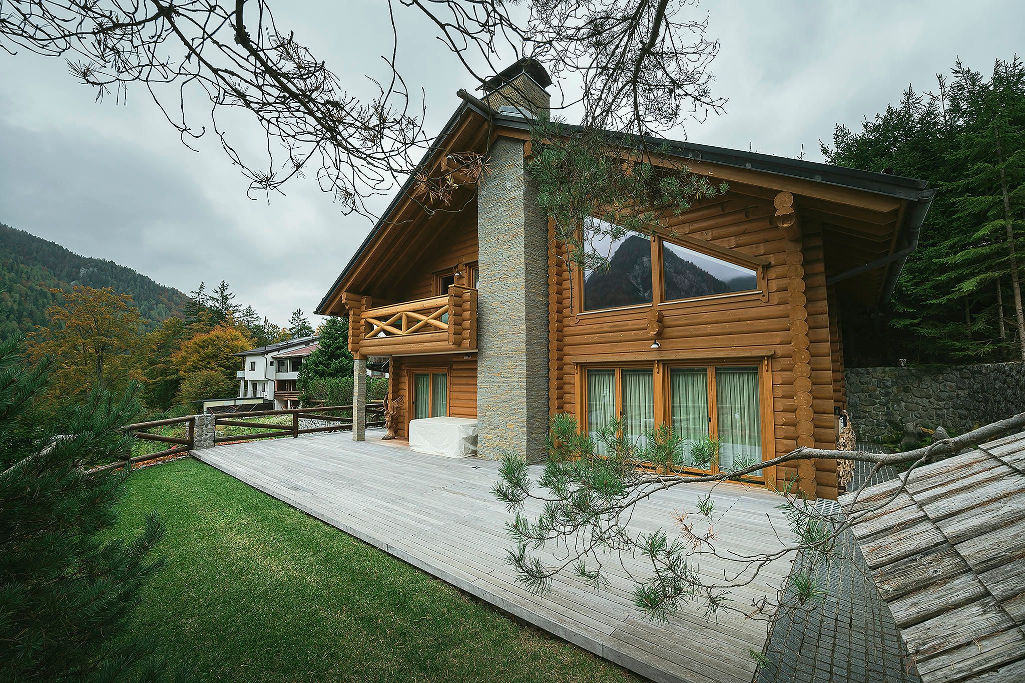 The whole chalet seen from the lawn, showing the full gable end, a stone chimney, large windows, and surrounding trees.