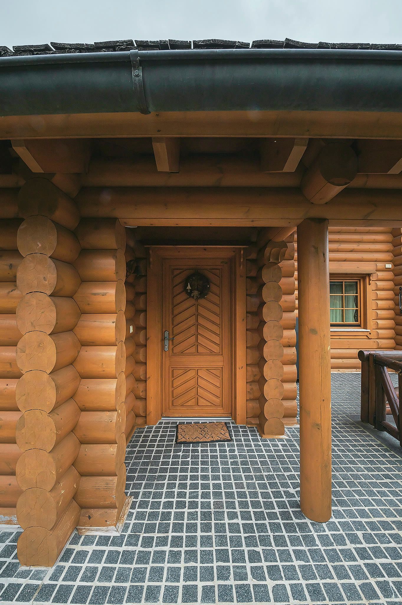 The chalet's carved timber front door set in a deep log-framed porch, with patterned stone paving underfoot.