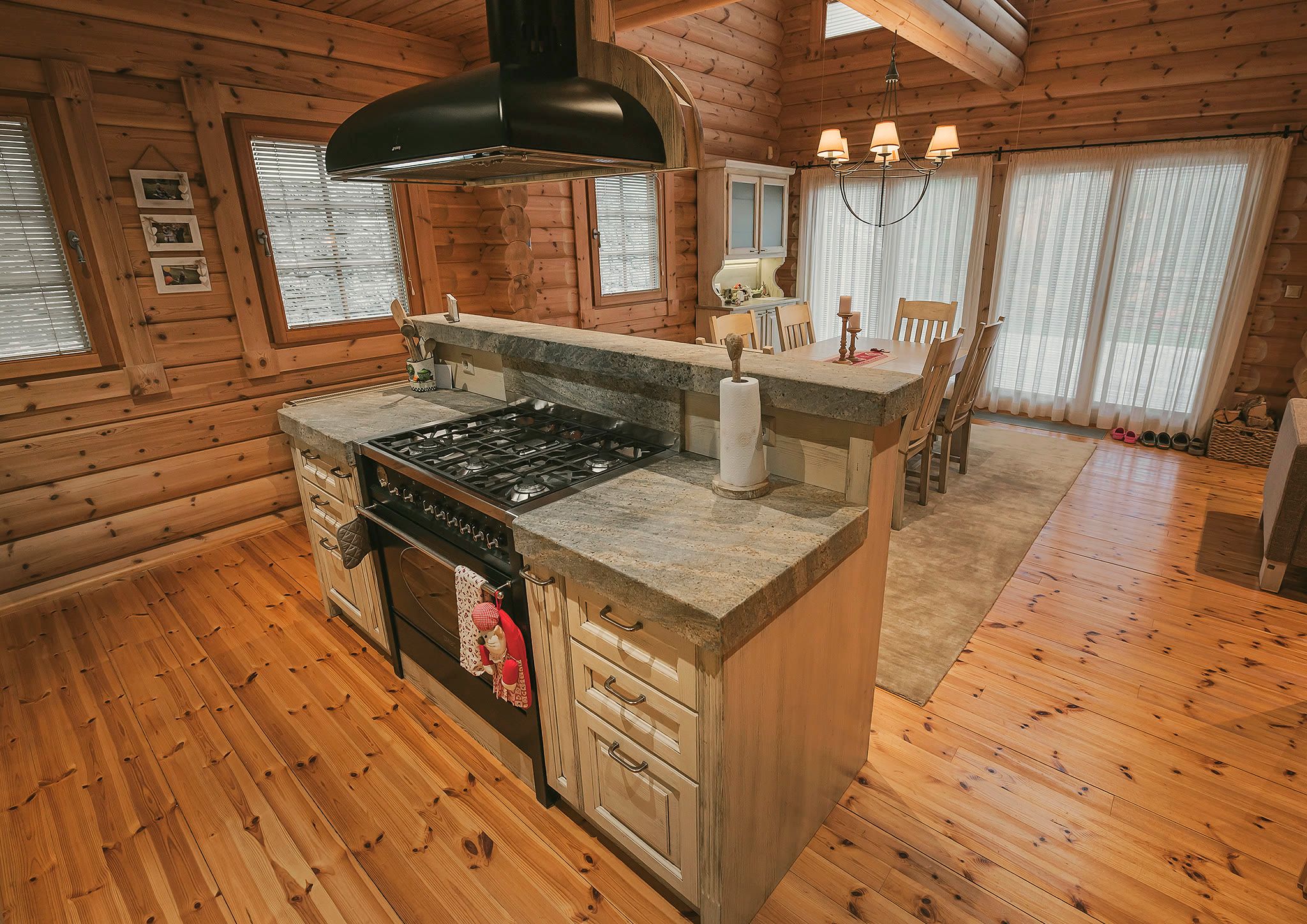 The kitchen island with a gas range and extractor hood, a stone counter, and a window beyond.
