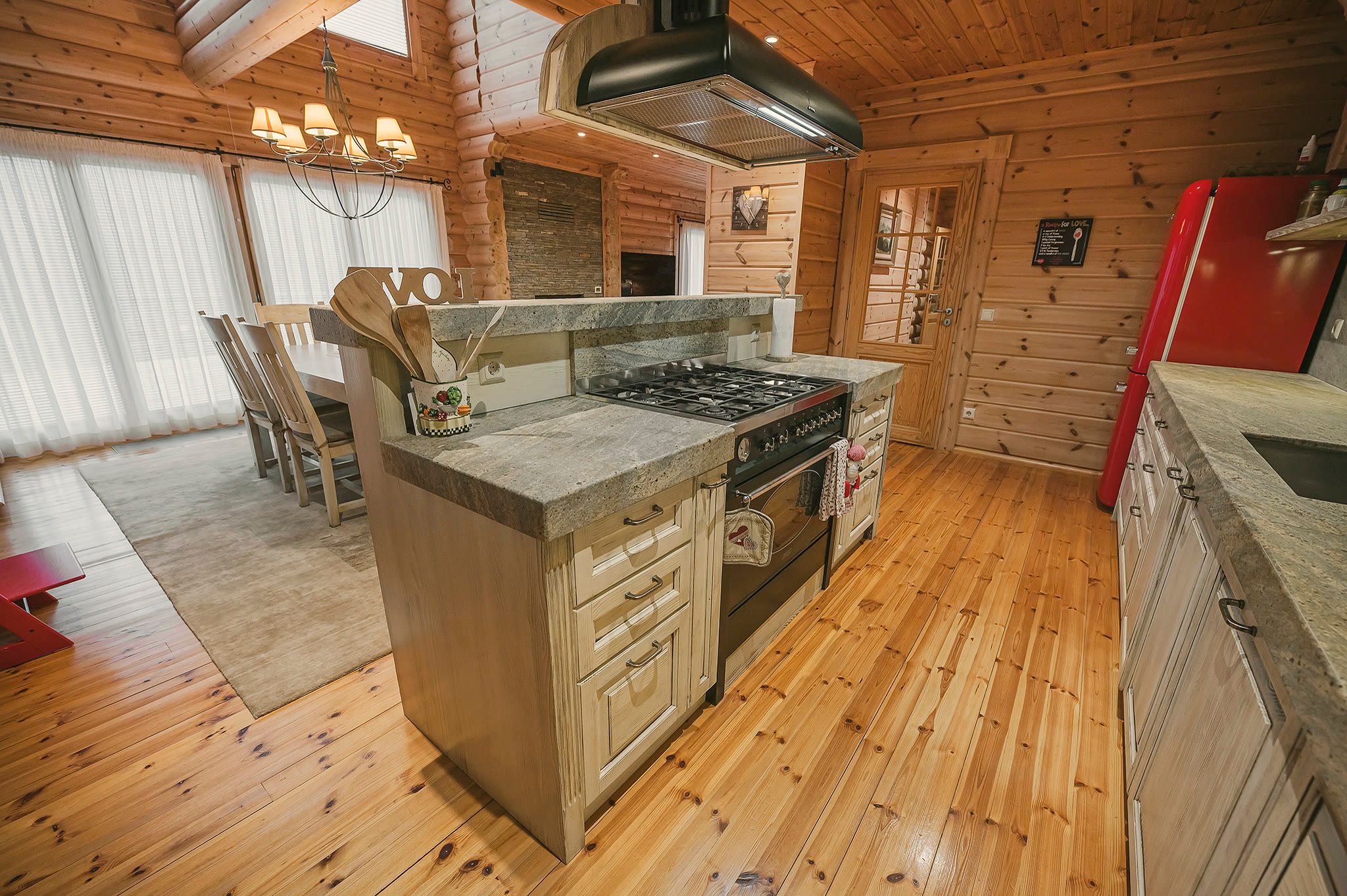 A wide view of the kitchen showing the island, gas range, red fridge, and round-log walls.