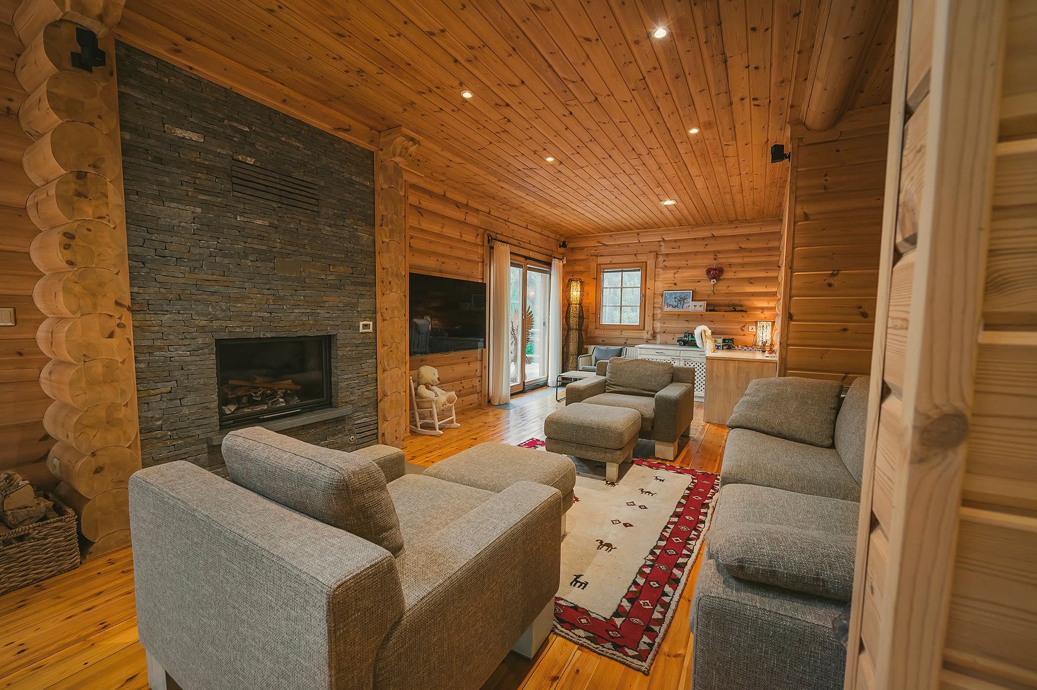 The living room with the stone fireplace lit, sofas, a TV, and round-log walls.