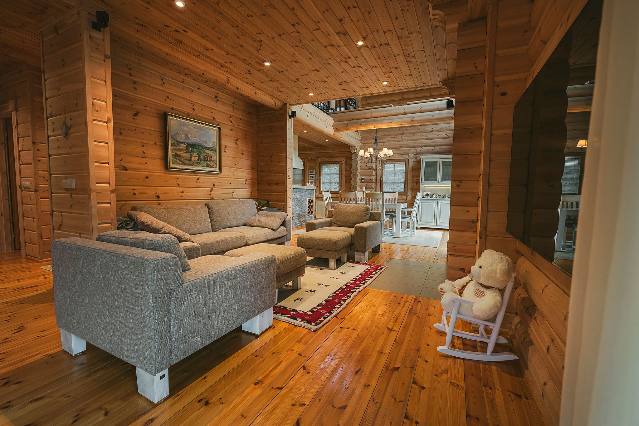 The living room with grey sofas, a rug, and a timber floor, opening onto the dining area beyond.