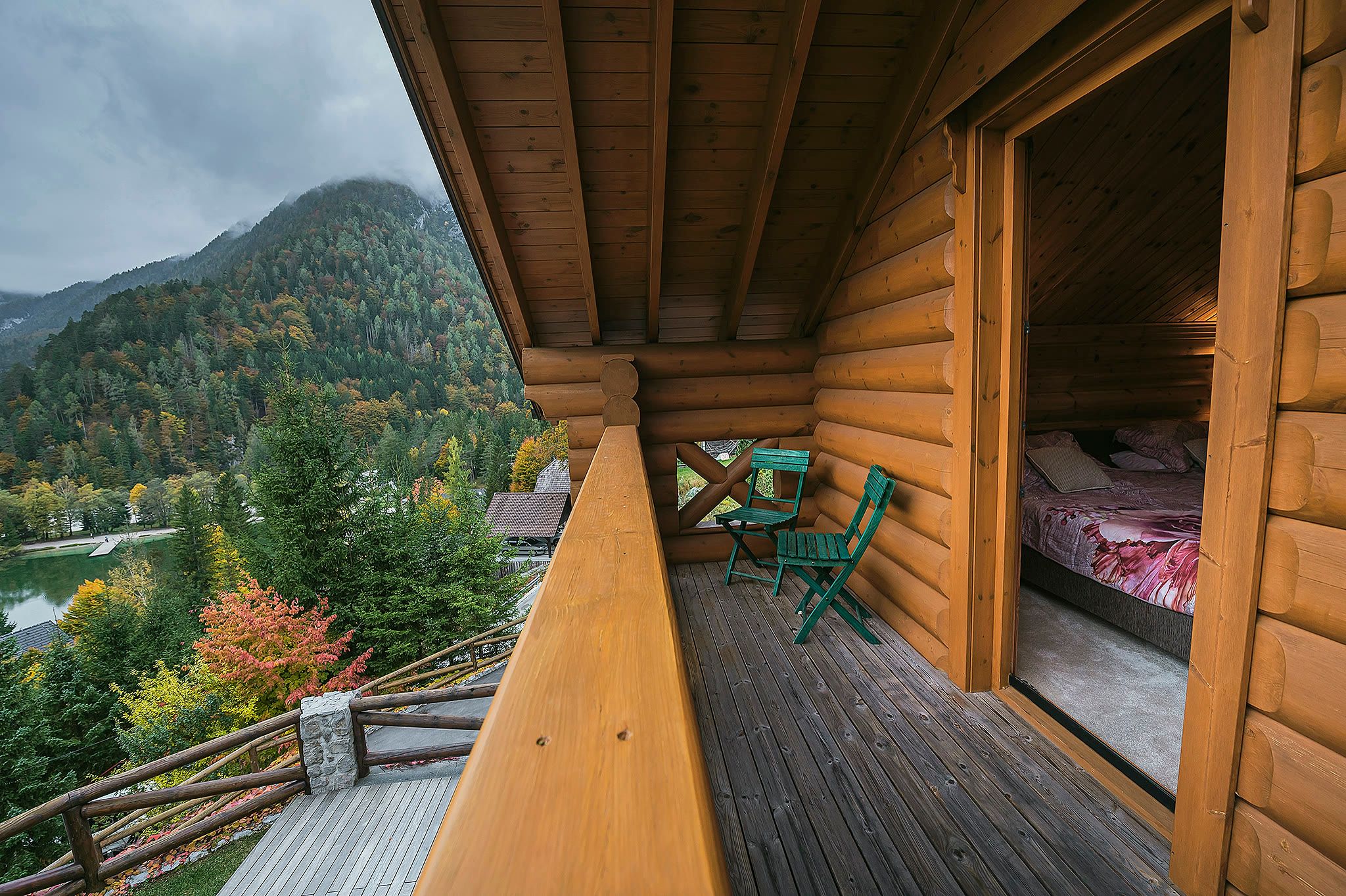 The master balcony with timber decking, a green chair, a log wall, and mountains and the lake edge beyond.