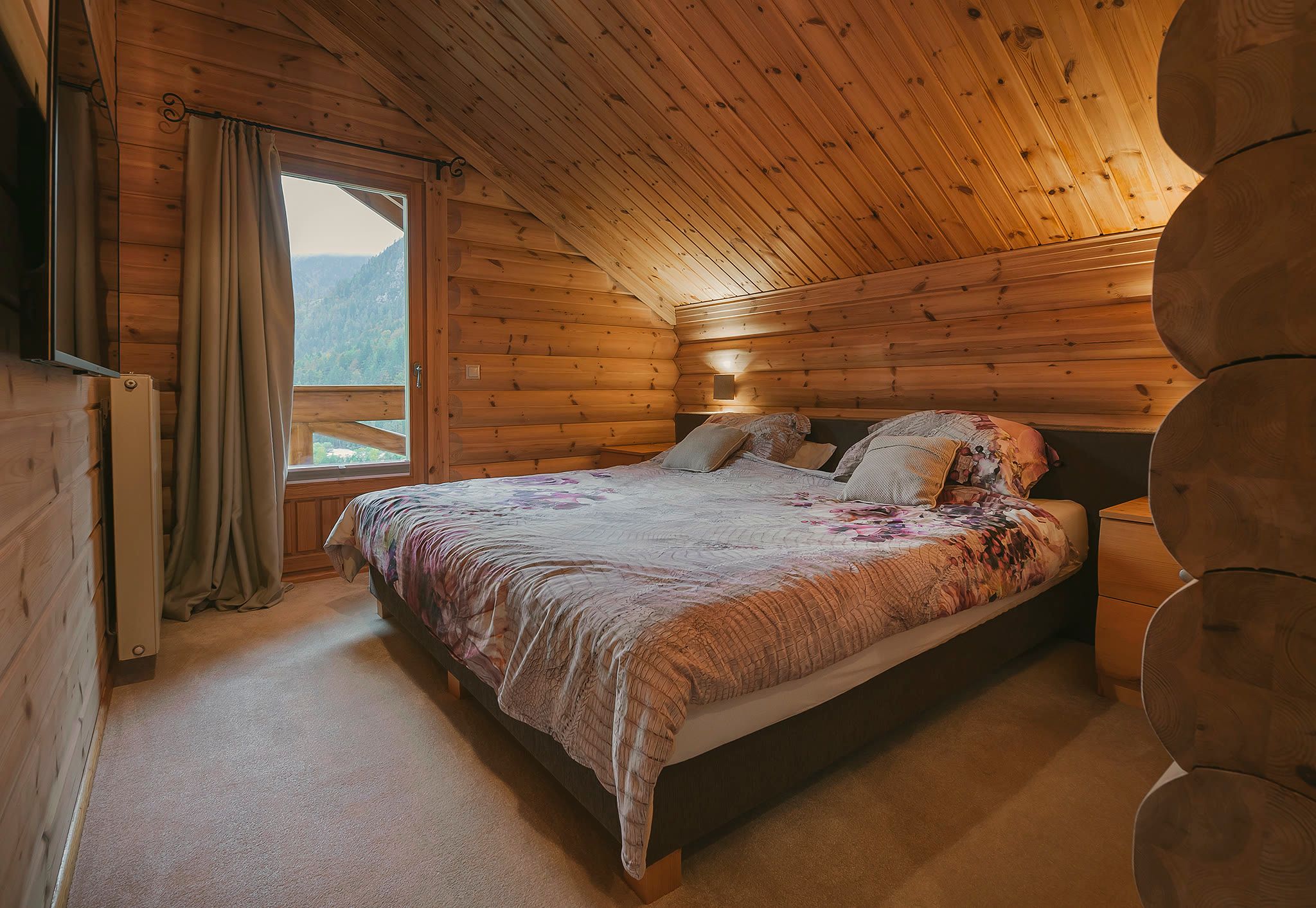 The master bedroom with a double bed, patterned bedding, a window facing the mountains, and a TV.