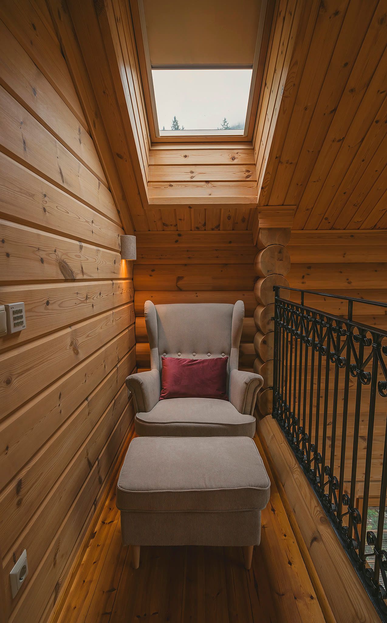 The gallery reading nook, with a wingback armchair and footstool beneath a skylight and a wrought-iron balustrade.