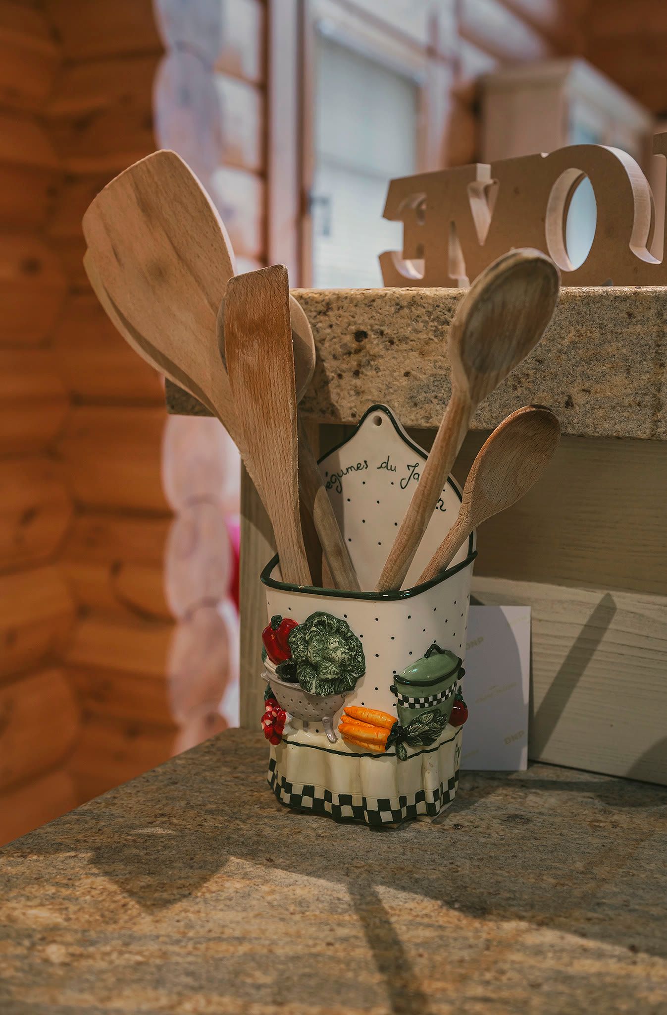 Wooden kitchen utensils standing in a painted ceramic crock.