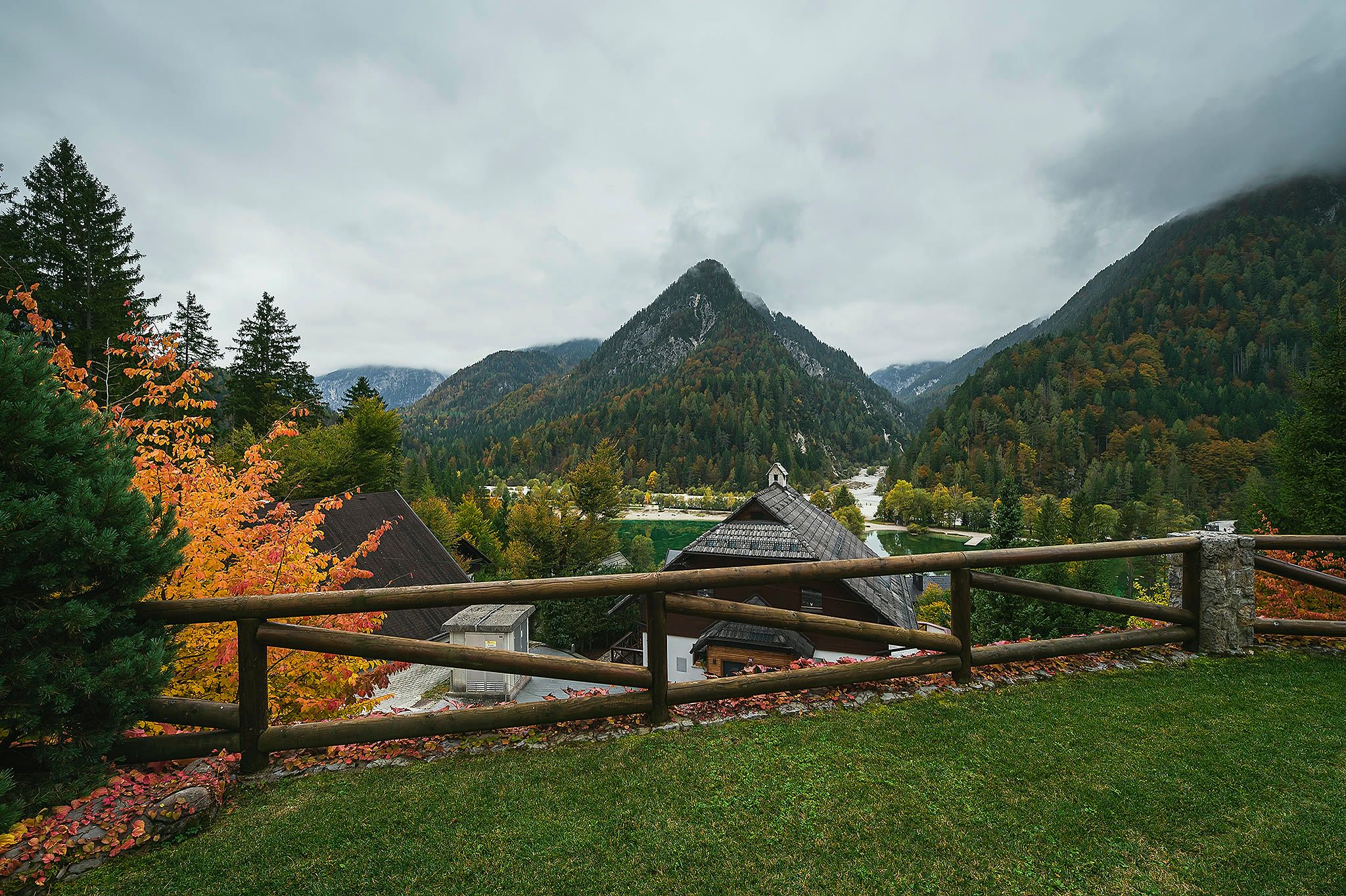 The view from the lawn across a timber fence and autumn trees to the valley and a sharp mountain peak beyond.